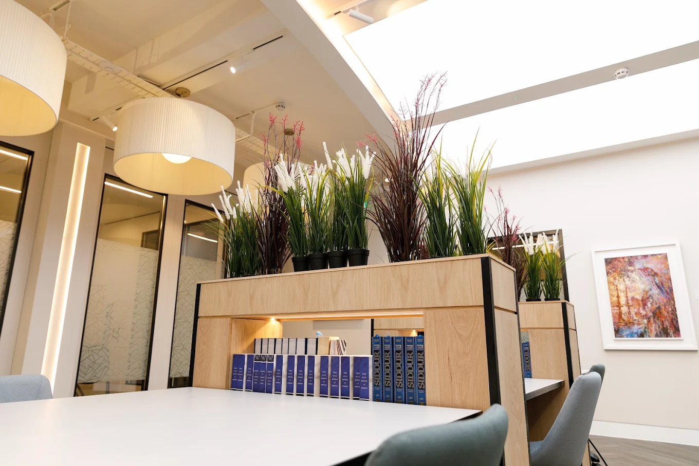 A table and upholstered chairs beside a planted timber bookshelf at Chabad HGS