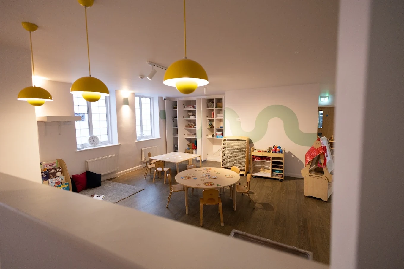 Nursery room with yellow pendant lights, small tables and low storage